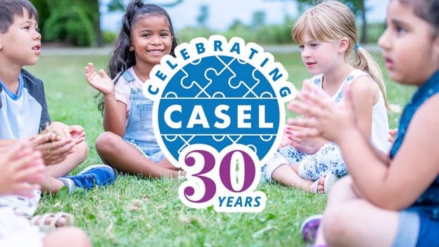 Happy children sitting in a circle outside with the logo for CASEL's 30th anniversary in the foreground