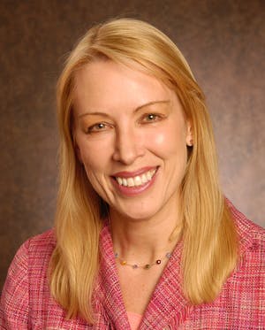 Mary Utne - a light skinned woman with straight yellow hair wearing a pink textured blazer and a beaded necklace. 