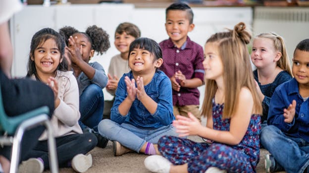 Happy kid in a classroom, sitting on rug and clapping